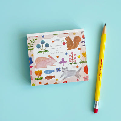 The Feel Nature memo pad by Aiko Fukawa on a blue background, next to a pencil for scale.