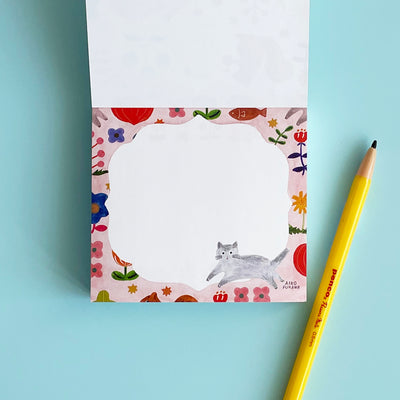 The memo pad is opened to a page featuring a grey cat and a mauve floral border.