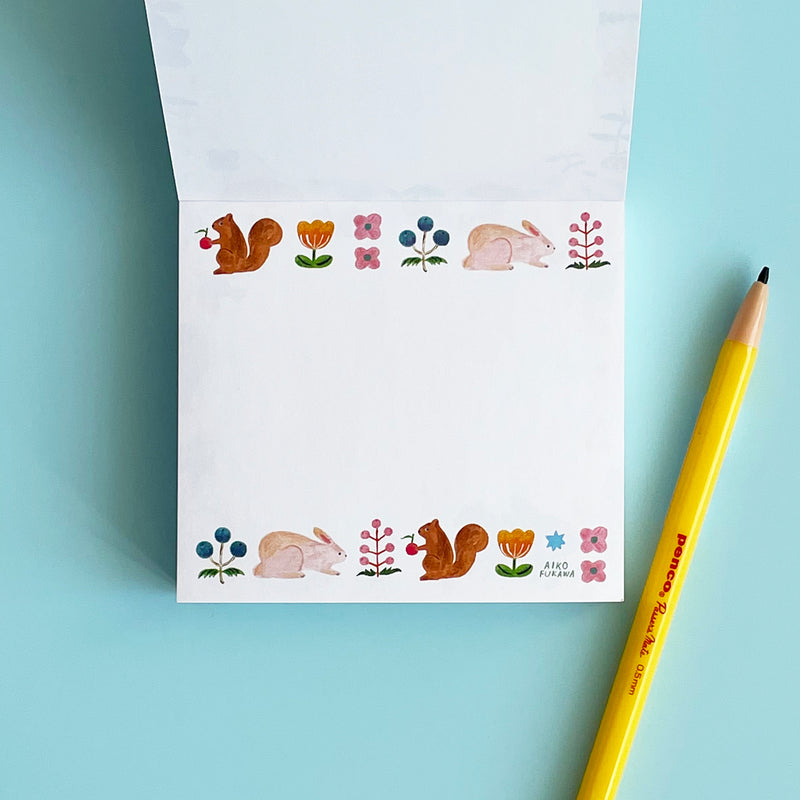 The memo pad is opened to a page featuring a border on the top and bottom of the white paper, with rabbits, squirrels, berries, and flowers.