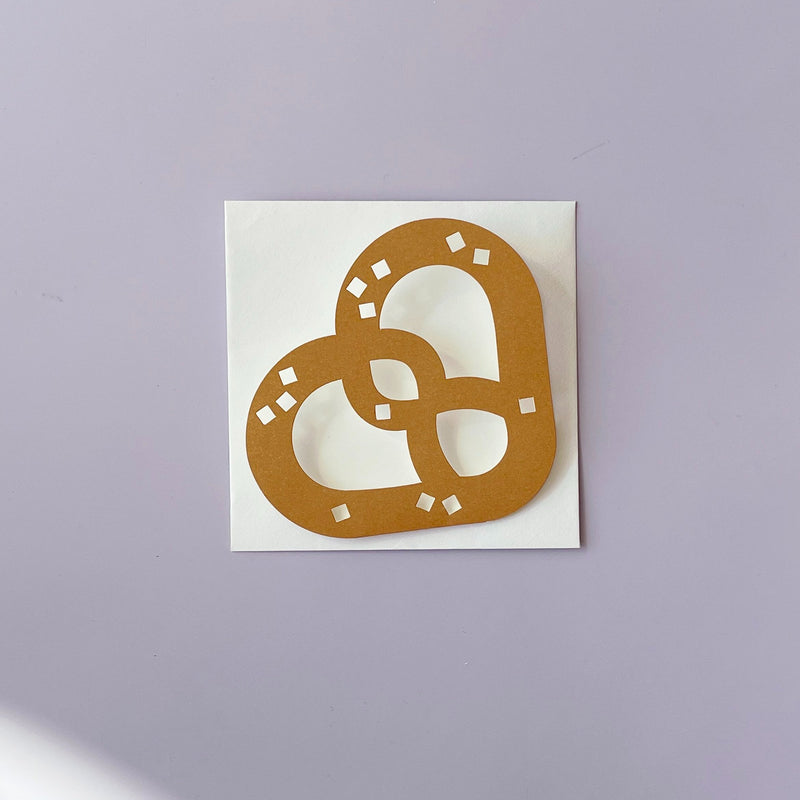 A brown pretzel shaped greeting card sitting on top of a white envelope. 