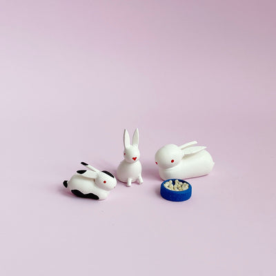 Three small white wooden bunny figurines on a light pink background.