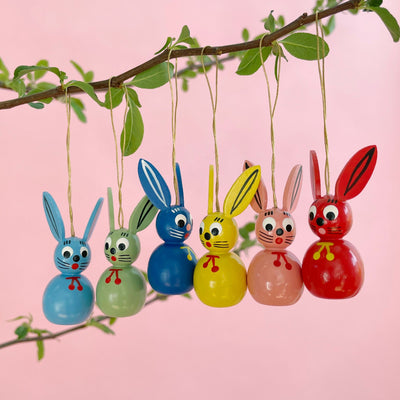 Six handpainted bunny ornaments hanging on a branch on a pink background.