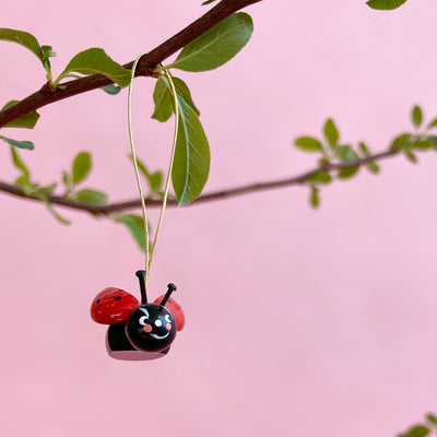 Wooden ladybug ornament hanging from a branch on a pink background.