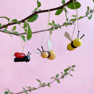 Wooden bug ornaments hanging from a branch on a pink background.