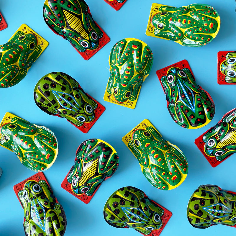 Several green tin frog clicker toys arranged on a light blue background. 