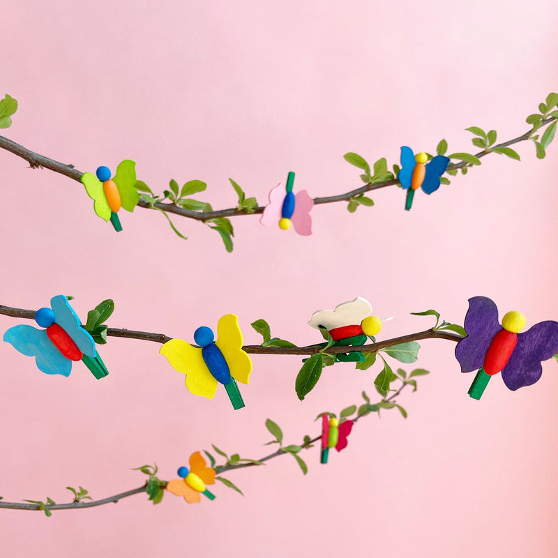 Colorful wooden butterfly clips clipped onto a branch against a pink background. 