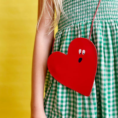 Red heart shaped purse being worn by a child in a green gingham dress
