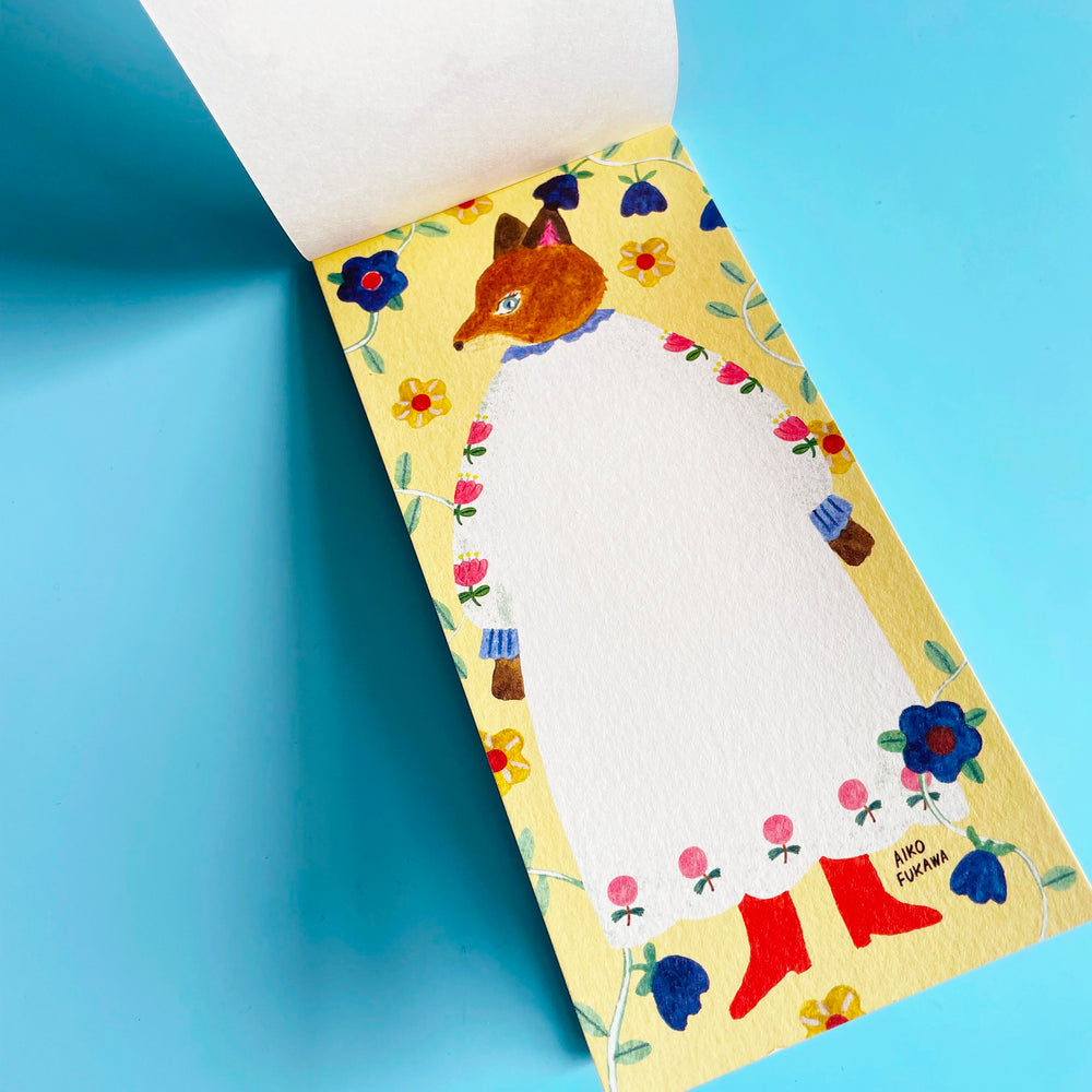 The memo pad is opened to a page featuring a anthropomorphic fox standing in a white dress on a yellow floral background.