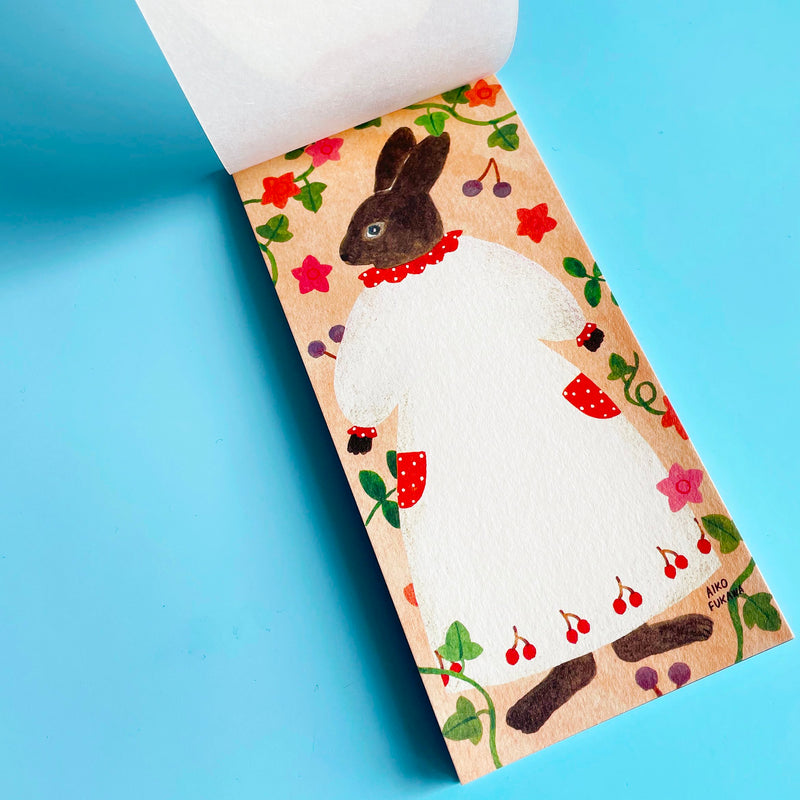 The memo pad is opened to a page featuring a anthropomorphic rabbit standing in a white dress with cherries on an amber background.
