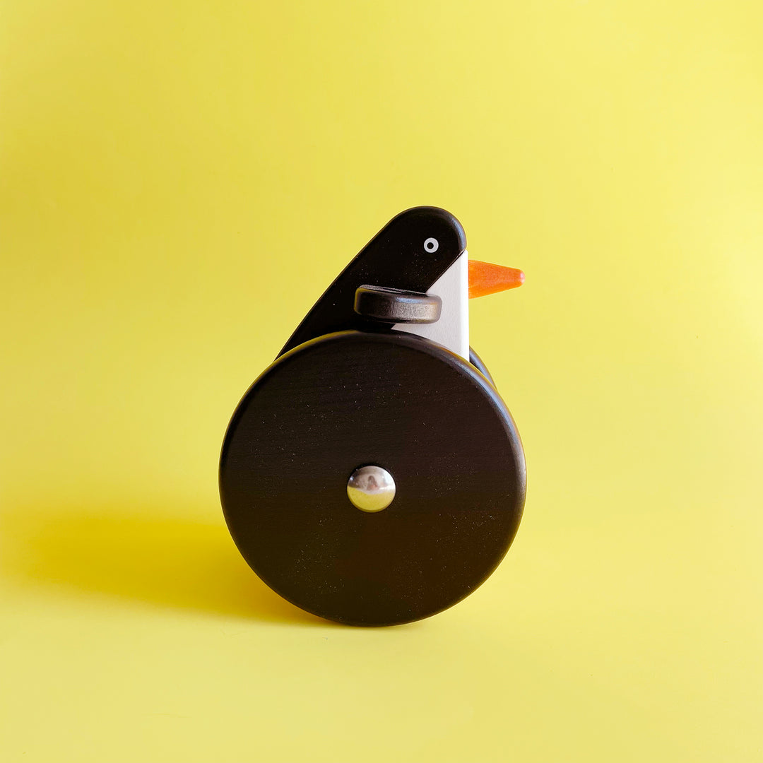 Rolling wooden penguin toy on a yellow background. 