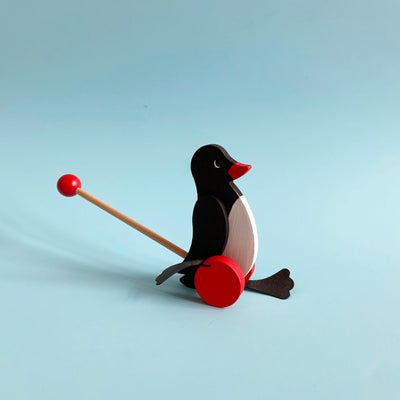 Small wooden penguin push toy on a light blue background.