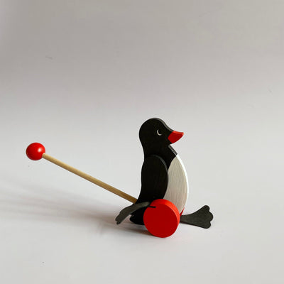 Small wooden penguin push toy on a cream colored background.