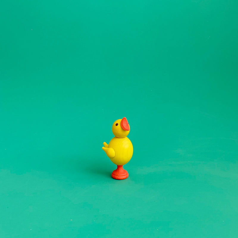 A small wooden chick figurine on a green background. 