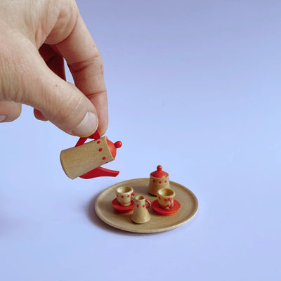 Small wooden red tea set, with a large hand pretending to pour the tea kettle. 